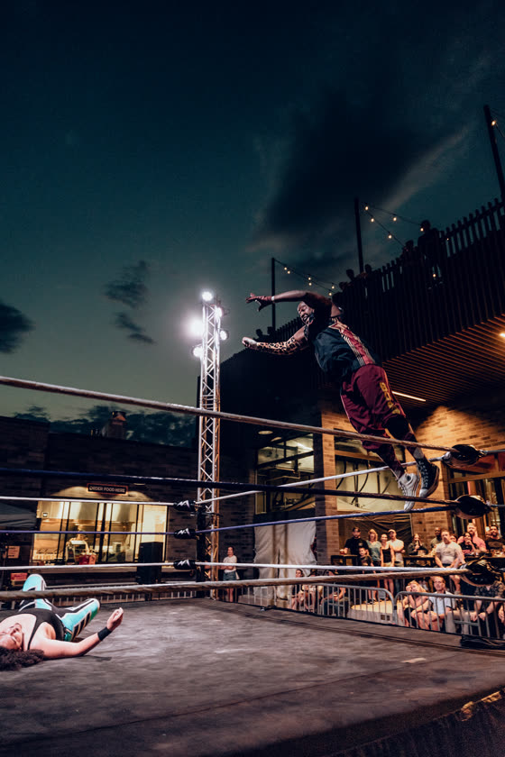 Wrestler launching off the top rope at an outdoor match